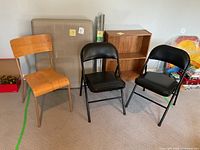 Wood chair, two black folding chairs, folded beige table, small bookcase, rolled blinds