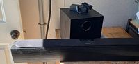 Front view of Pioneer soundbar resting on table edge, Pioneer subwoofer behind with power adapter atop