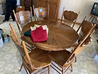 round oak pedestal table with six chairs and folded tablecloths on top