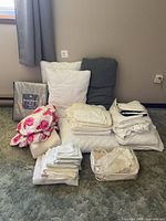 Full view of assorted bedding items—pillows, packaged set, stacked sheets, floral piece, towels