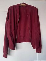 Front view of burgundy lightweight jacket on hanger showing zipper, ribbed collar, cuffs, hem