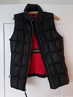 Front view of black quilted puffer vest open to show red lining