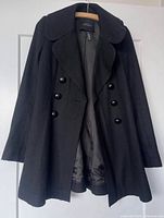 Front view of black double-breasted peacoat hanging on hanger