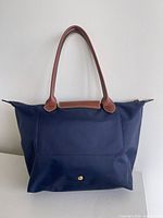 Front view showing navy body, brown leather handles and snap pocket