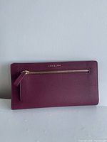 Front of plum Love & Lore travel wallet showing gold-tone zipper pocket and logo
