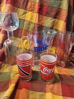 Group shot of pitcher, novelty wine glass, bar menu glass, and two Coca-Cola tumblers