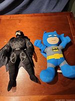 Both Batman plush dolls side by side on table surface