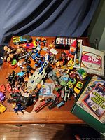 Overview of mixed toys spread on table including TMNT, Transformers, vehicles, plush and trains
