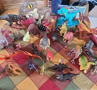 Group of assorted loose dinosaur figures displayed on blanket with two larger figures nearby