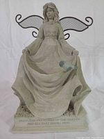Front view of ceramic statue planter showing figure, dish, bird accent and inscription on base