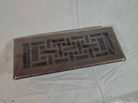 Top view of one shrink-wrapped copper brushed vent cover with geometric cutout
