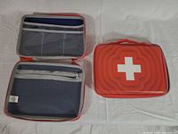 Two red first aid cases, one closed showing white cross emblem, one open displaying interior mesh pockets