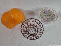 Three bowls viewed from top: orange glass, bronze wire with beads, porcelain floral compote