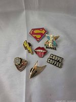 Front view of all seven enamel pins on cloth background