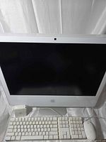Front view of white Apple iMac with screen off, keyboard, mouse, power adapter visible