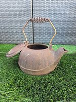 Side view of rusted cast iron teapot with open hinged lid and wire handle showing spring grip