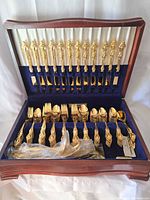Open wooden chest displaying gold-plated knives, forks, spoons in blue velvet interior