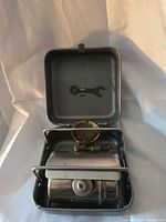 Stove open showing brass burner, steel tank, interior, wrench clipped inside lid