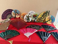 Overall lot of 18 folding fans displayed on red cloth