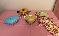Group shot of all three casserole dishes with lids, two metal stands, and folded floral linens