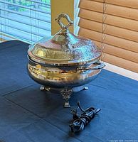 Full view of silver-plated casserole server with lid on and power cord beside