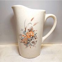 Full view pitcher front showing shape, cream speckled finish, floral design