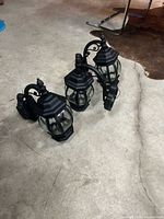 Three matching black metal outdoor wall lanterns on concrete floor