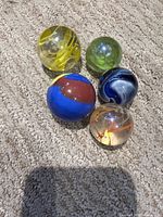 All five marbles grouped on carpet showing size differences and color patterns