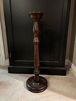 Full view of dark wood pedestal stand against black cabinet