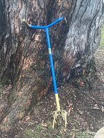Full view of blue and yellow Garden Claw cultivator leaning against tree