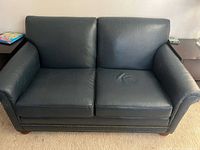 Full front view of black leather loveseat showing overall design, cushions, nailhead trim, and feet