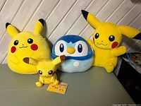Four Pokémon character plush toys: three Pikachu and one Piplup displayed on table