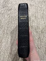 Spine view showing black textured leather cover and gold title Prayer Book