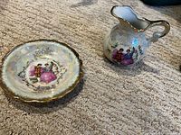 Small porcelain cream pitcher and matching plate with courting couple motif and gold trim