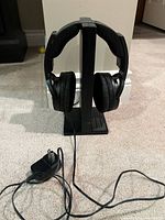 Headphones seated on vertical transmitter/charging stand with attached cable and power adapter visible
