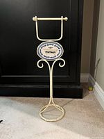 Entire toilet paper holder showing metal frame, base, spindle and decorative ceramic plaque