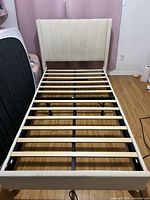 Full view of bed frame without mattress, showing upholstered headboard, side rails, footboard, and wooden slats