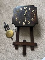 Front view of wall clock with detached pendulum, key and wooden piece
