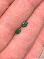 Both oval emeralds on fingertip showing size and cut
