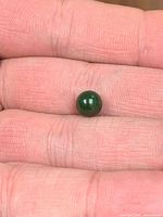 Dark green jade bead resting on fingertip, showing size and polish