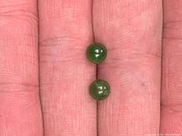 Pair of small olive-green jade beads on fingertips