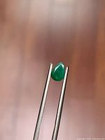 Pear-cut emerald held by tweezers, showing full face of stone