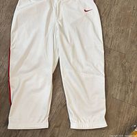 Front view of full-length white pants showing red Swoosh and side stripe