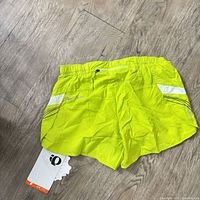Front view of lime neon yellow Pearl Izumi running shorts showing reflective accents and zipper pocket with tags attached