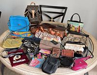 Group shot of seventeen assorted handbags and pouches laid out on round table