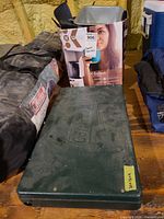 Closed green steel Coleman stove beside cookware box and tent bag