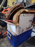 Blue Coleman cooler with box containing wicker items on top