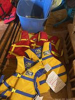 Two Fluid yellow-blue life jackets with tags, Buoy-O-Boy red-yellow jackets, blue bin