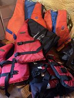 Stack of five life jackets showing red-black Qualifier and red/orange Buoy-O-Boy vests