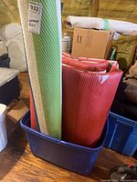 Rolled rugs standing in blue bin: green/blue/white rug and red/white rug